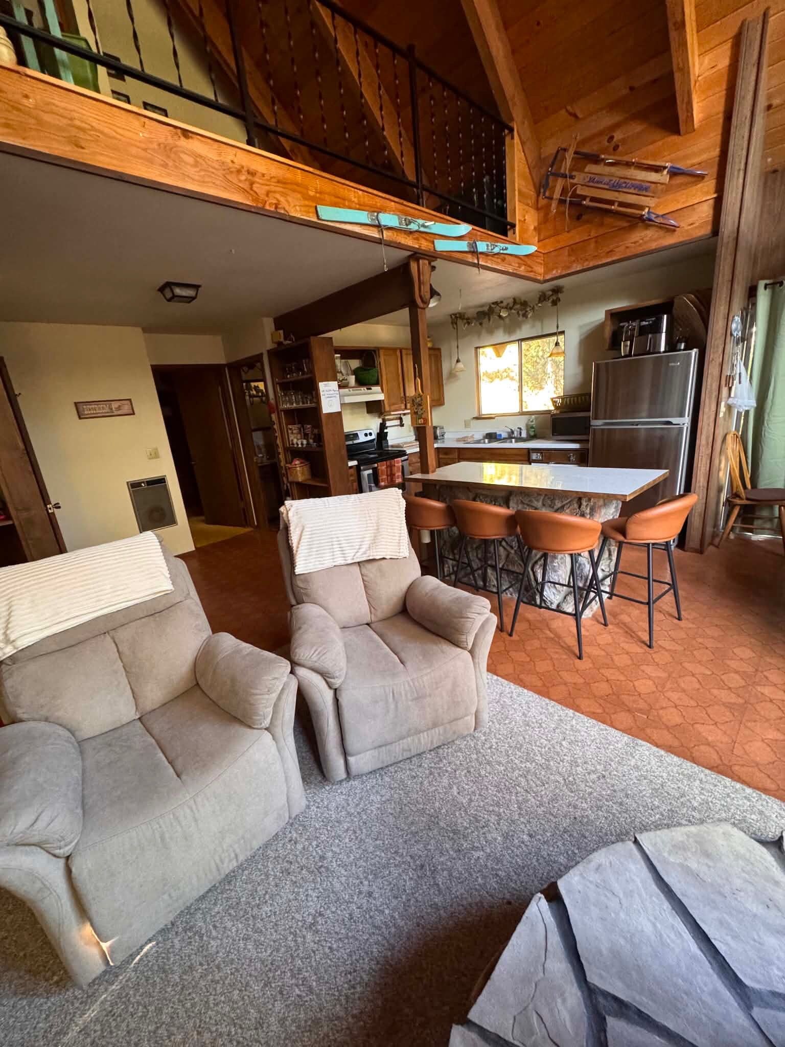 Un salon confortable avec un canapé, un fauteuil et une petite table. Il y a également un coin cuisine équipé d’un réfrigérateur et d’une table à manger.