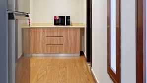 Een smalle gang met houten vloeren, een keuken met een koelkast en magnetron, en een deur aan de rechterkant.