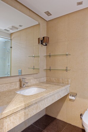 A bathroom with a beige marble countertop, a white sink, a large mirror, and a glass shelf unit. - VESTA - Luxury APT - 2BR - New Cairo (II) (New Cairo City)