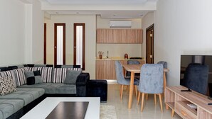 Een moderne woonkamer met een grijze bank, een salontafel, en een eethoek met een houten tafel en stoelen.