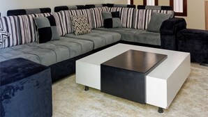 Een moderne woonkamer met een hoekbank, een salontafel en een groot raam met gordijnen.