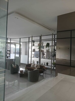 A modern living room with a sofa, armchairs, and a coffee table. There are shelves with decorative items and plants. - Cozy 2-bedroom condo with AC and Pool in beautiful Santo Domingo (Santo Domingo)