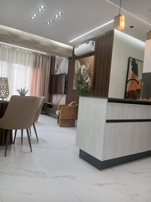 A modern living room with a central island, a dining area with chairs, and a large window with curtains. - Cozy 2-bedroom condo with AC and Pool in beautiful Santo Domingo (Santo Domingo)