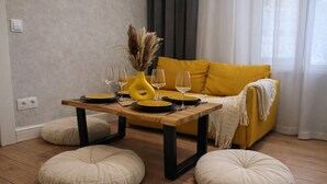 Ein Essbereich mit einem Holztisch, gelben Kissen und einer gelben Vase mit getrockneten Pflanzen.