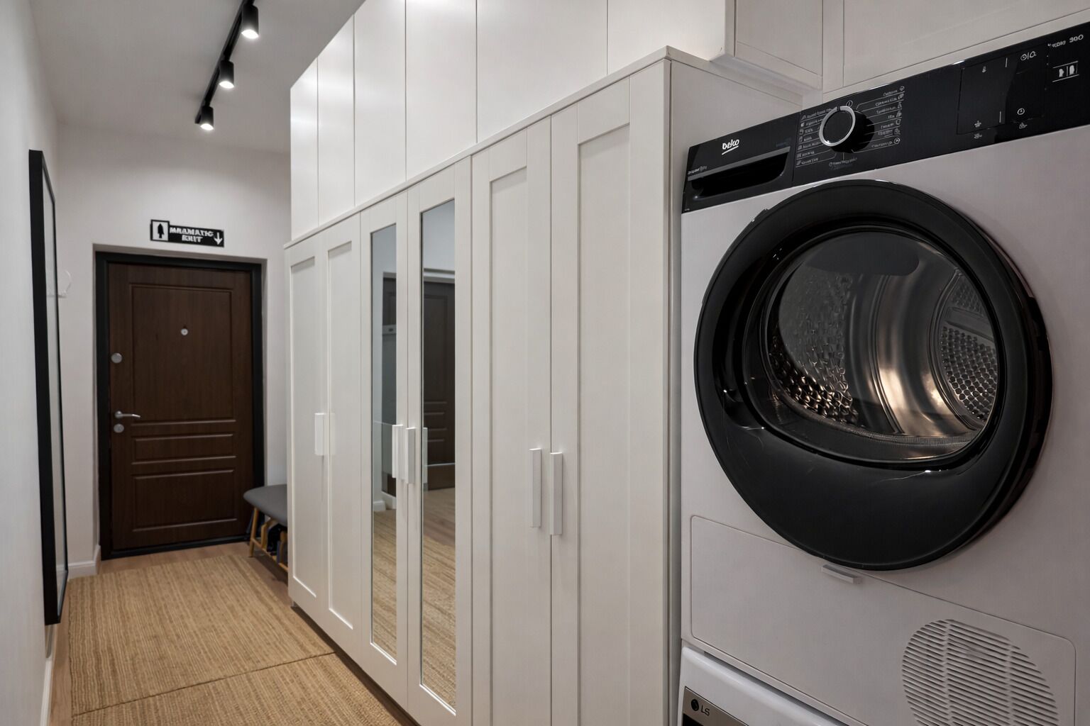 Une buanderie équipée d’un lave-linge à chargement frontal, d’une porte en bois et d’un meuble avec une porte-miroir.