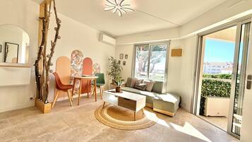 Ein modernes Wohnzimmer mit einer Couch, einem Couchtisch und Sesseln, ein Essbereich mit Tisch und Stühlen, eine Zimmerpflanze und Blick durch eine Schiebetür.