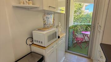 Eine kleine Küche mit Mikrowelle, Toaster und einem kleinen Mülleimer. Eine Glastür öffnet sich zu einem Außenbereich mit Tisch und Stühlen.