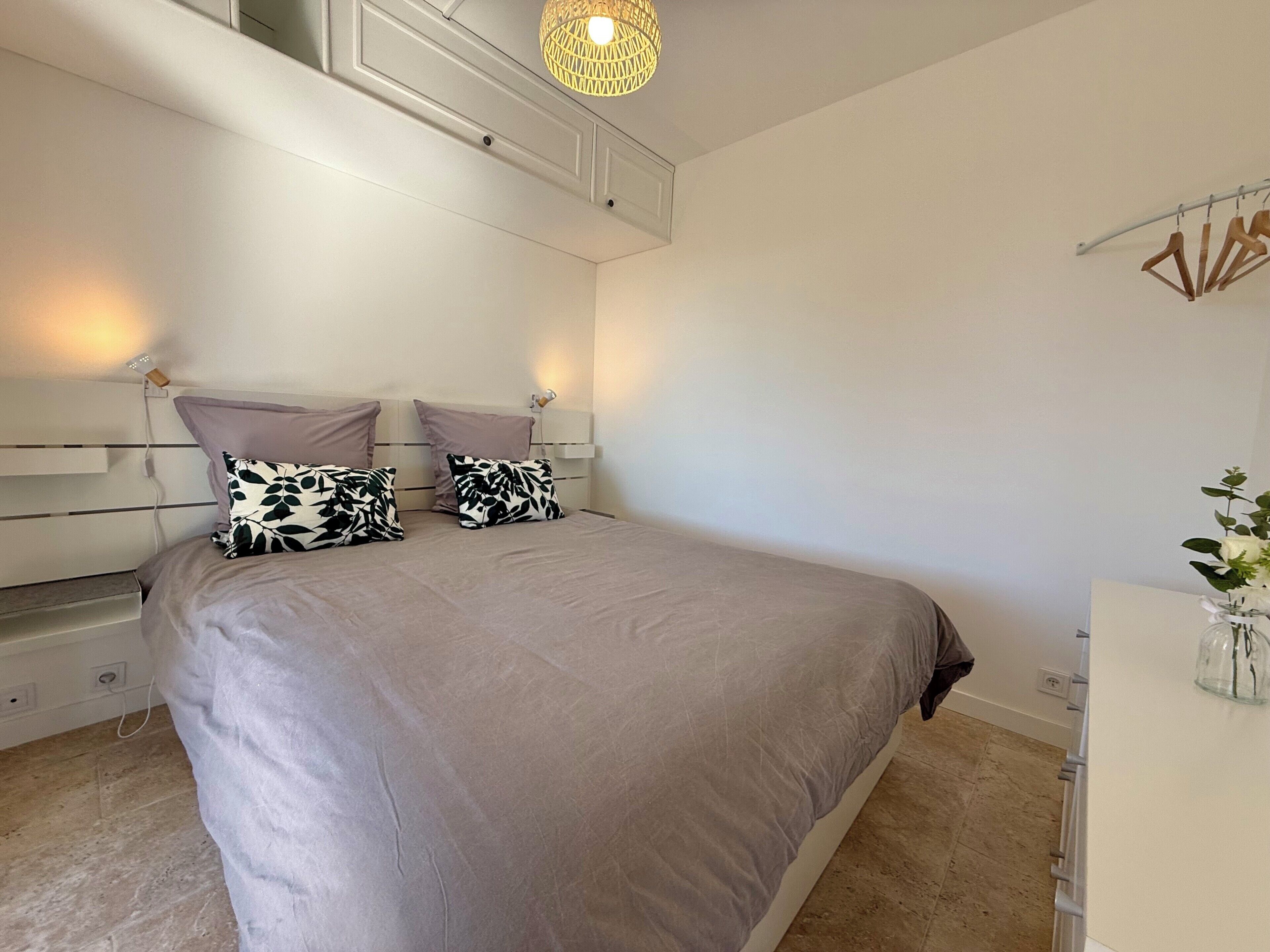 Ein Schlafzimmer mit Bett, Nachttischen, einem Schminktisch, einer Pendelleuchte und einem Wandregal.