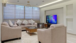 A modern living room with a beige sofa, two armchairs, a coffee table, and a TV on a stand. - VESTA - Luxury APT - 2BR - Heliopolis (Al Golf)