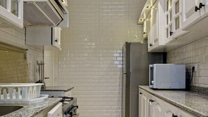 A narrow kitchen with white cabinets, a stainless steel refrigerator, a microwave, and a gas stove. - VESTA - Luxury APT - 2BR - Heliopolis (Al Golf)