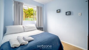 Camera da letto con un letto, un comodino, una finestra con tende e vista sul verde.