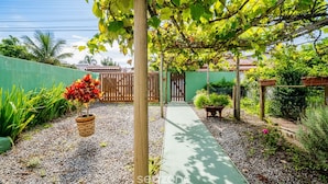 Un giardino con vialetto in ghiaia, pergola in legno e piante in vaso.