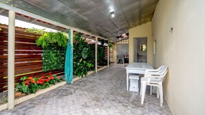Un patio coperto con pavimento piastrellato, un tavolo con sedie e un recinto in legno con piante.