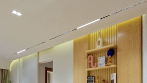 Uma sala de jantar moderna com mesa de vidro e cadeiras estofadas, parede de madeira com prateleiras e uma porta visível que dá para outro cômodo.
