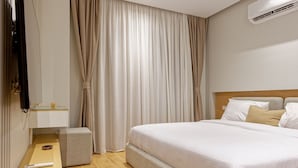 Quarto de hotel com cama, mesa de cabeceira, televisão e cortinas.