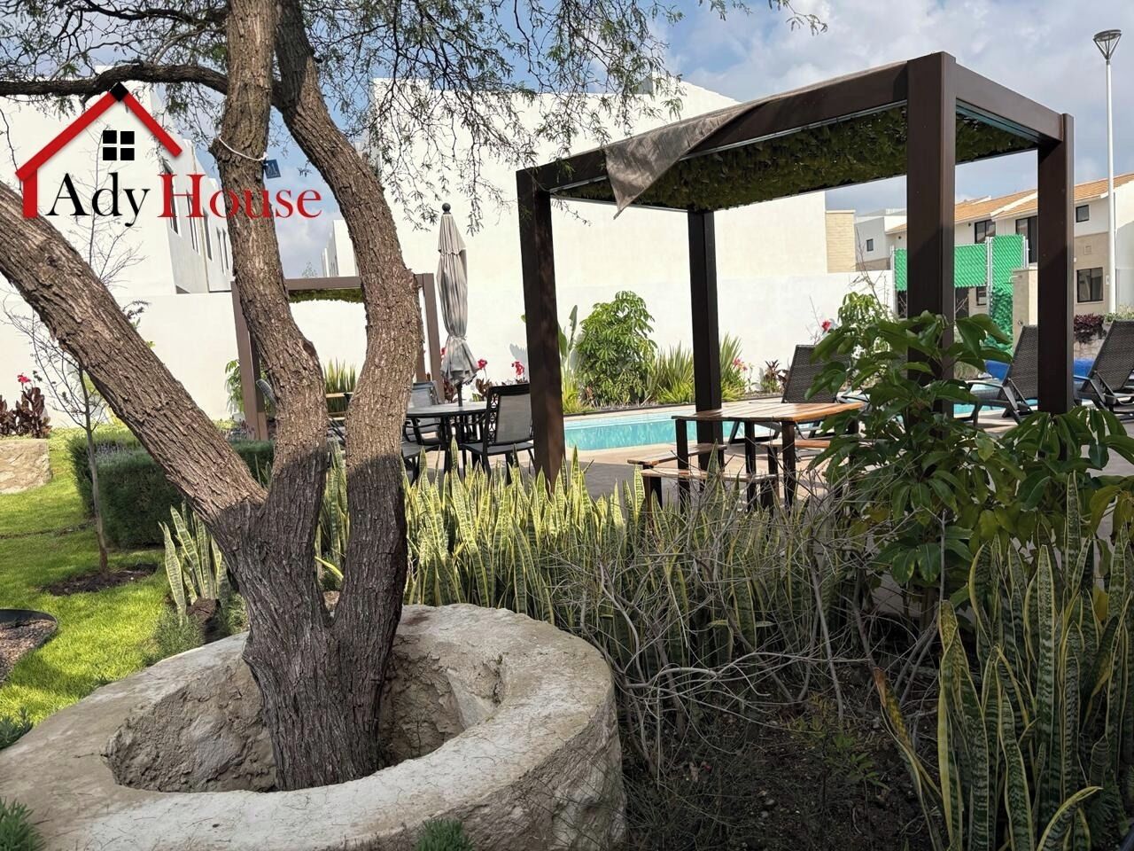 A garden area with a gazebo, outdoor seating, and a swimming pool in the background.