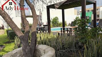 A garden area with a gazebo, outdoor seating, and a swimming pool in the background.