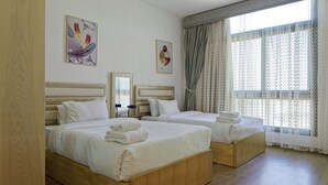 Une chambre d’hôtel avec deux lits en bois, du linge de lit blanc, une grande fenêtre avec des rideaux légers et deux œuvres d’art accrochées au mur.