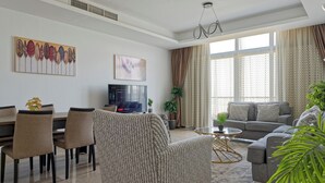 Un salon moderne comprenant un canapé, un fauteuil, une table à manger, des chaises, un téléviseur et une grande fenêtre avec des rideaux.