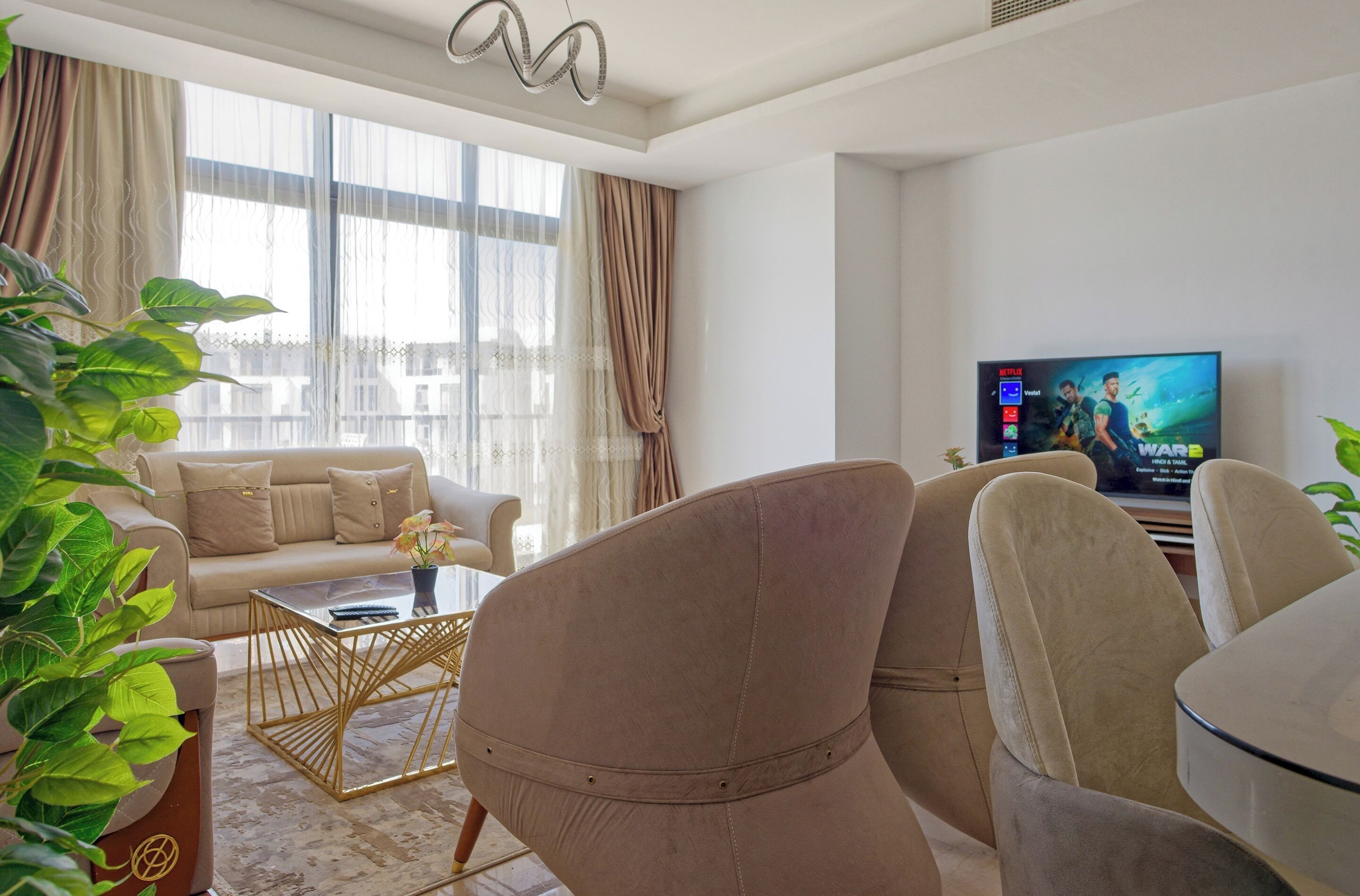 Un salon moderne avec un canapé beige, une table basse en verre et un téléviseur diffusant un film.