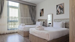 Een hotelkamer met twee bedden, een groot raam met gordijnen en kunstwerken aan de muur.