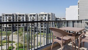 Een balkon met rieten meubels, met uitzicht op een woongebied met moderne gebouwen en palmbomen.