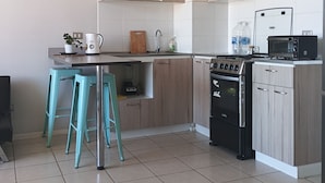 Una cocina moderna con armarios de madera clara, una estufa negra, un microondas y dos taburetes turquesa.