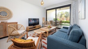 A modern living room with a blue sofa, wicker chairs, a wooden coffee table, and a flat-screen TV.