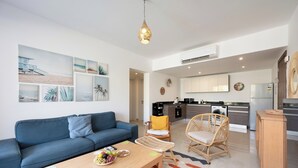 A modern living room with a blue sofa, a wooden coffee table with fruits, a wicker chair, and a kitchen in the background.