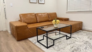 Ein Wohnzimmer mit einem braunen Ledersofa, einem Glastisch und einem gemusterten Teppich.