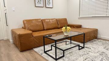 A living room with a brown leather sofa, a glass coffee table, and a patterned rug.