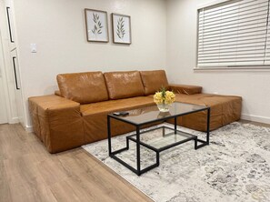 Ein Wohnzimmer mit einem braunen Ledersofa, einem Glastisch und einem gemusterten Teppich.
