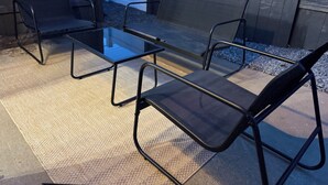 Eine Terrassenfläche mit einem Glastisch und vier schwarzen Stühlen.