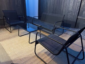 Eine Terrassenfläche mit einem Glastisch und vier schwarzen Stühlen.