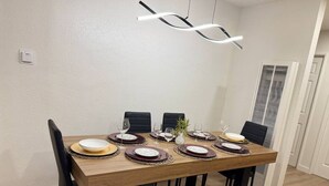 Ein Essbereich mit einem rechteckigen Holztisch, gedeckt für sechs Personen, schwarzen Stühlen und einer modernen Pendelleuchte.