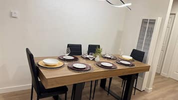 Un coin repas avec une table rectangulaire en bois, disposée pour accueillir six personnes, des chaises noires et un luminaire suspendu au design moderne.