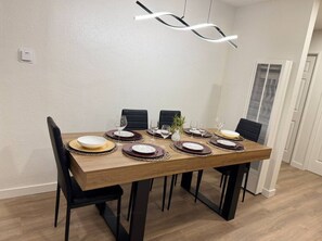 Ein Essbereich mit einem rechteckigen Holztisch, gedeckt für sechs Personen, schwarzen Stühlen und einer modernen Pendelleuchte.