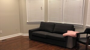A room with a dark wood floor, a gray sofa, a black chair, and a ceiling fan. - 2-bedroom townhome in superb Baltimore with parking and gated yard (Baltimore)