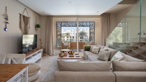 A modern living room with a sofa set, a TV, a dining table, and a balcony with a view of buildings. - VESTA - Luxury APT - 2BR - Mangrovy (El Gouna)