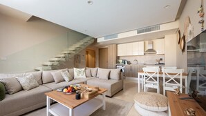 A modern living room with a sofa, coffee table, and dining area. A staircase leads to an upper level. - VESTA - Luxury APT - 2BR - Mangrovy (El Gouna)