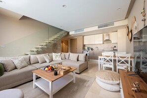 A modern living room with a sofa, coffee table, and dining area. A kitchen is visible in the background. - VESTA - Luxury APT - 2BR - Mangrovy (El Gouna)
