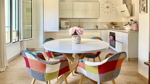 Een moderne keuken met witte kasten, een ronde eettafel en kleurrijke stoelen.