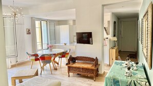 Een moderne woonkamer met een bank, een eettafel met kleurrijke stoelen, een houten bankje en een aan de muur bevestigde televisie.