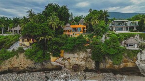 A coastal property with a thatched-roof structure, a modern building, and lush greenery.