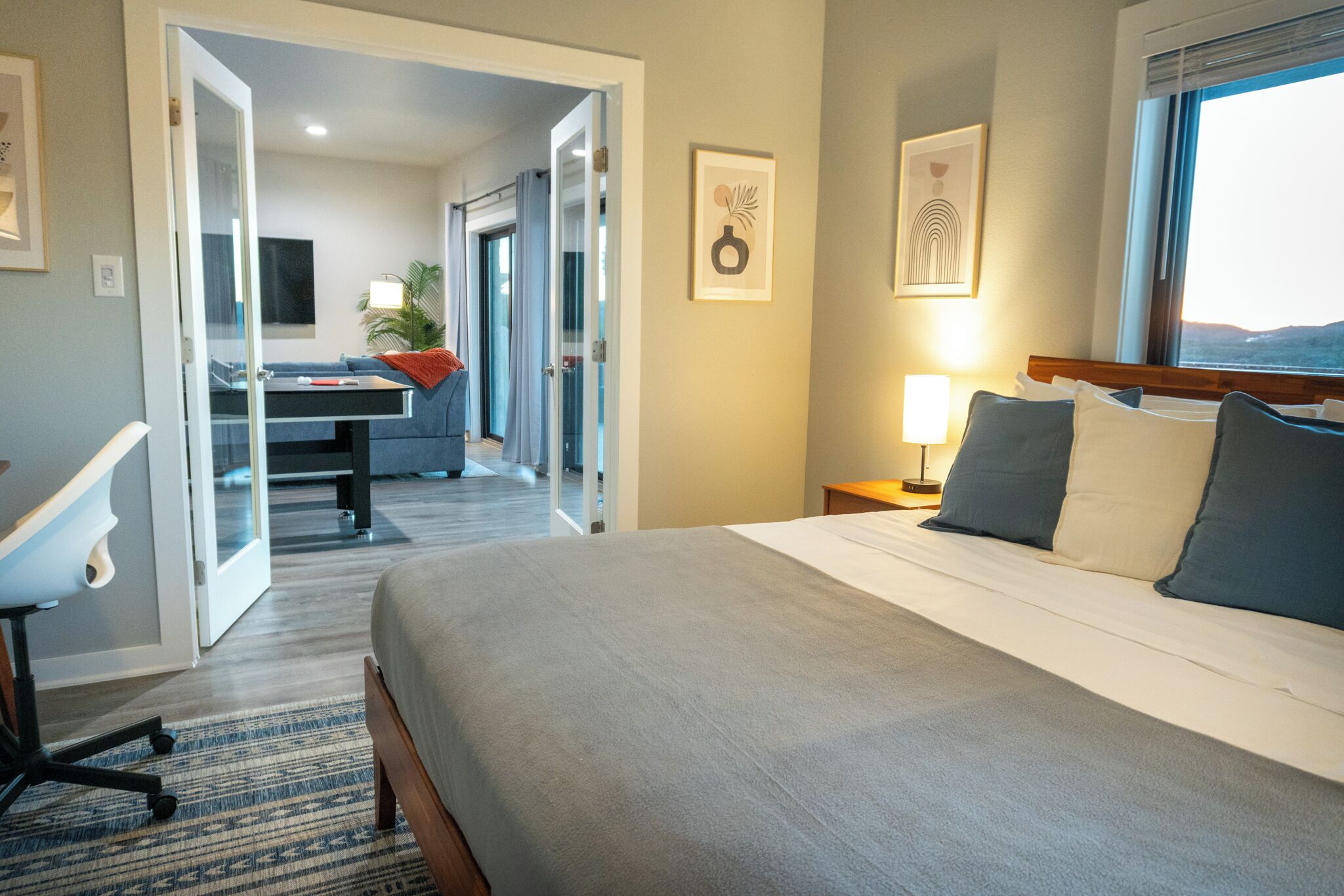 A hotel room with a large bed, a desk, a chair, and a view of the outdoors.