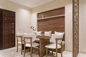 A dining area with a glass-top table, four upholstered chairs, a wooden cabinet, and a decorative wall panel. - VESTA  - Luxury APT - 2BR - La Mirada (I) (New Cairo City)