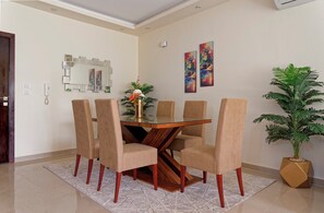 A dining area with a glass-top table, six beige chairs, a vase of flowers, and two abstract paintings on the wall. - VESTA  - Luxury APT - 2BR - La Mirada (II) (New Cairo City)