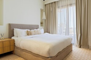 A neatly made bed with a headboard, a bedside table with a lamp, and a view of the outdoors through sheer curtains. - VESTA - Luxury APT - 1BR - Fairway (El Gouna)