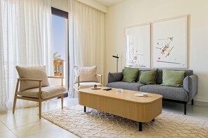 A living room with a sofa, two chairs, a coffee table, and artwork on the wall. - VESTA - Luxury APT - 1BR - Fairway (El Gouna)