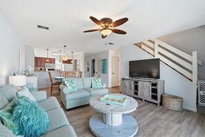 A spacious living room with a ceiling fan, a dining area, and a kitchen in the background.